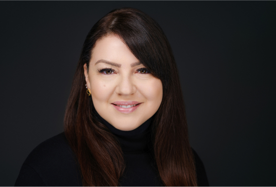 A brunette woman with long hair in a black turtleneck.