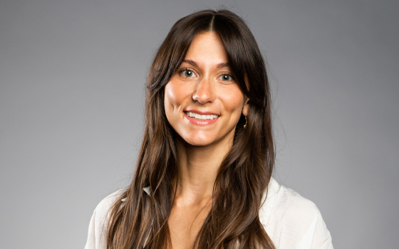 A brunette woman with long hair in a white cardigan.