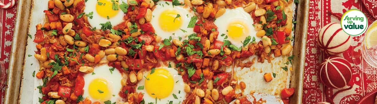 Baking sheet pan of bacon, beans and eggs breakfast on a set table with a red patterned tablecloth.