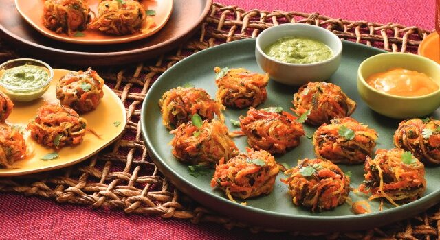 A big plate filled with Bhaji and two small dips, two full smaller plates, and two full glasses with wheat stalks as decoration.