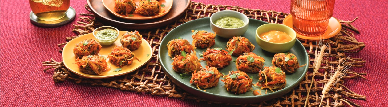 A big plate filled with Bhaji and two small dips, two full smaller plates, and two full glasses with wheat stalks as decoration.